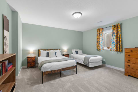 A well-decorated bedroom with a queen bed and a twin bed, bright curtains, and a bookshelf.