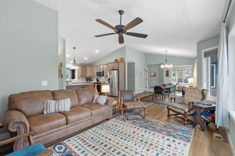 A cozy living room featuring a brown leather sofa, colorful rug, and an open kitchen area.