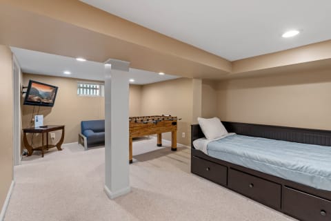 A recreational basement room featuring a foosball table, daybed, and a TV.