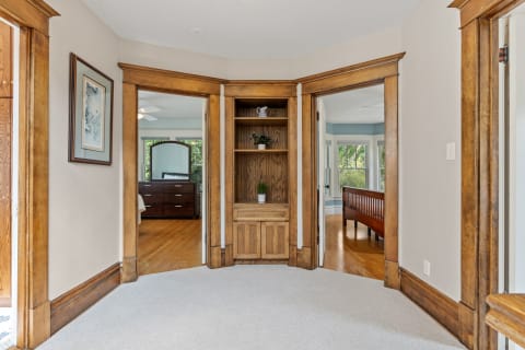 Interior view of a home with wooden trim, carpeted floor, and a built-in shelf in a corner.