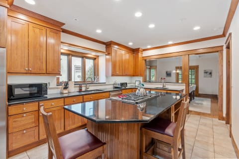 A kitchen with polished wooden cabinets, a granite countertop island, and a cozy dining area visible in the background.