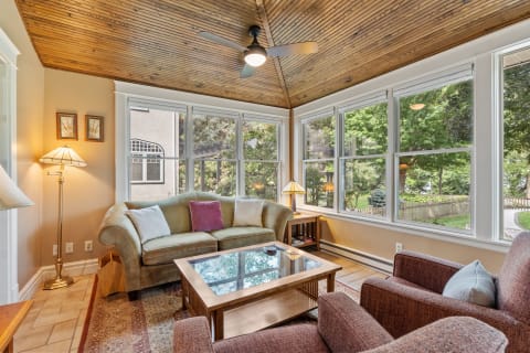 A sunroom with large windows, a green sofa, and a view of an outdoor landscape.