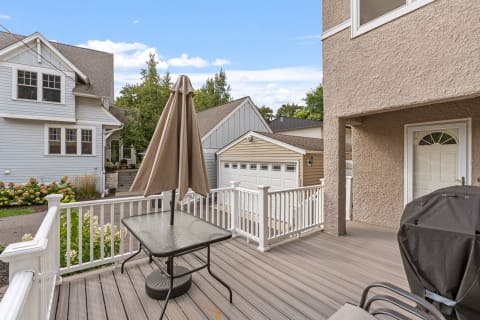 Outdoor deck with a table and umbrella overlooking homes and greenery.
