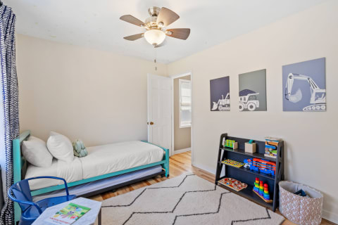A cozy children's bedroom with a bed, toys on shelves, and construction vehicle art.
