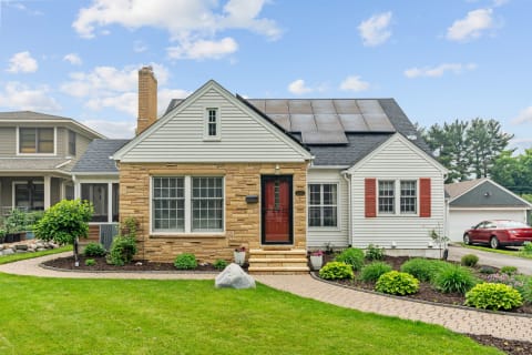 A house with stone and siding exterior, solar panels, and well-kept gardens in the front yard.