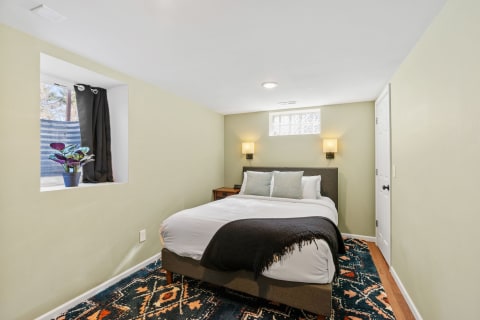 Cozy bedroom with a made bed, wall lamps, and a potted plant in the window.