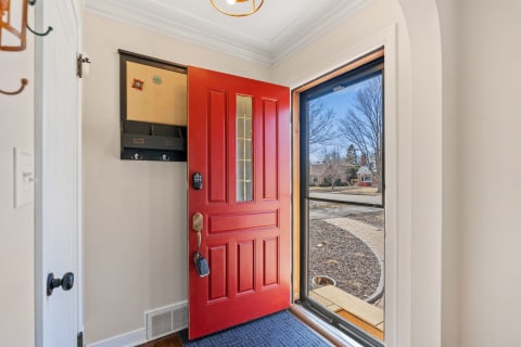 An entryway with an open red front door, wall-mounted organizer, and a view of the landscaped yard.