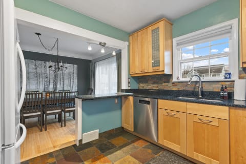 Interior view of a modern kitchen connected to a dining area, featuring granite countertops and wood cabinetry.