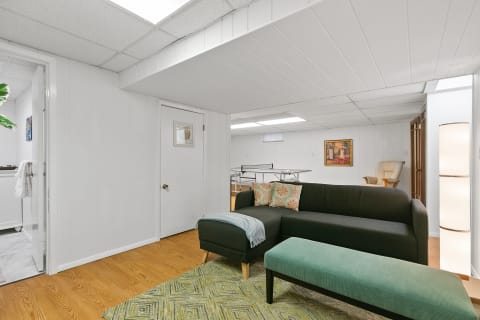 Cozy basement living room with a dark sofa, green ottoman, and wooden decor.