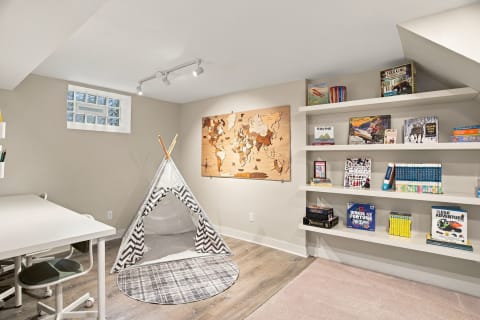 A play space with a teepee, bookshelves filled with games and books, and a wooden world map on the wall.