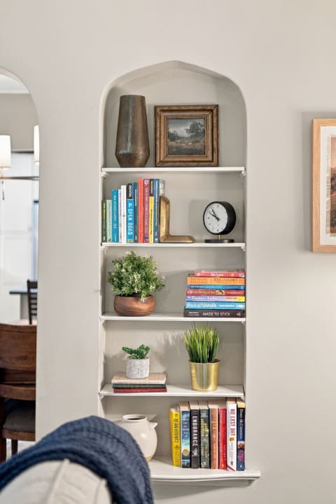 A built-in shelf featuring colorful books, plants, and decorative items in a cozy nook.