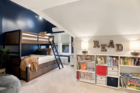 A cozy children's bedroom with a bunk bed, a reading nook, and colorful bookshelves.