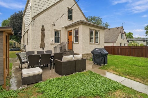An outdoor patio with wicker furniture, a dining area, BBQ grill, and lush lawn.