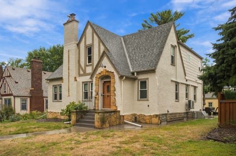 A Tudor-style home with a textured stucco facade, steep roof, and stone-accented entrance in a peaceful residential area.