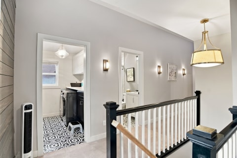 Upstairs hallway with gray walls, black and white patterned floor, and elegant lighting, leading to laundry and bathroom spaces.