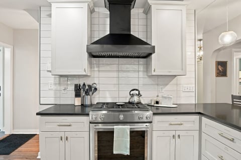 Modern kitchen featuring a stainless steel gas range, white cabinetry, and a dark countertop against a white tile backsplash.