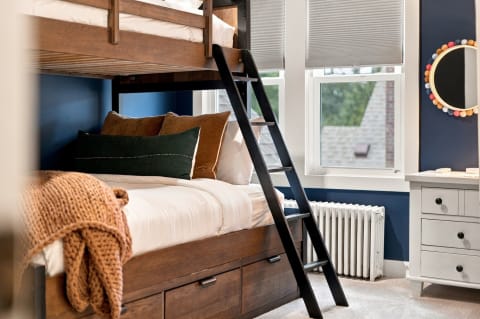 Cozy bunk bed featuring plush linens, a knitted blanket, and colorful decor in a blue room.