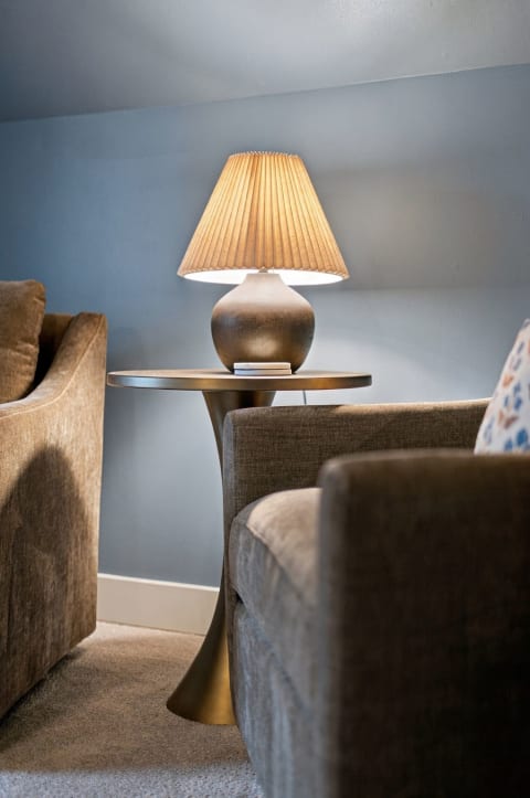 A soft-lit cozy seating area with a lamp, side table, and textured sofas against a blue wall.