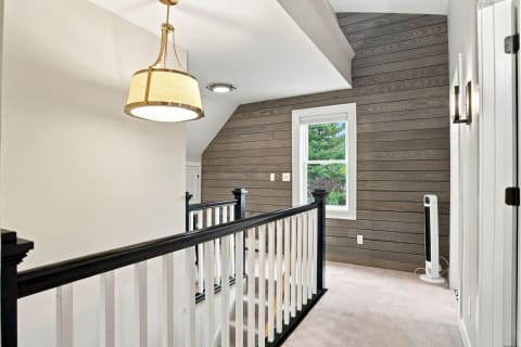 A cozy hallway featuring rustic wood paneling, elegant lighting, and a view of greenery through a window.