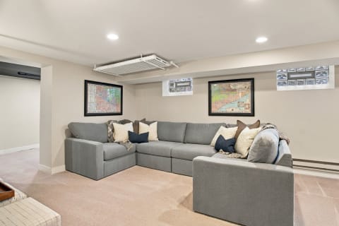 A stylish lower-level retreat with a spacious gray sectional sofa, decorative pillows, and framed maps on the walls.