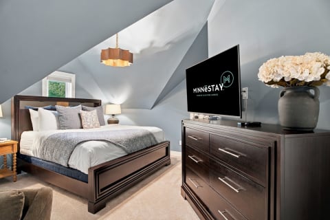 A cozy attic bedroom with a king bed, stylish lighting, and modern amenities, featuring blue walls and plush carpets for a relaxing retreat.