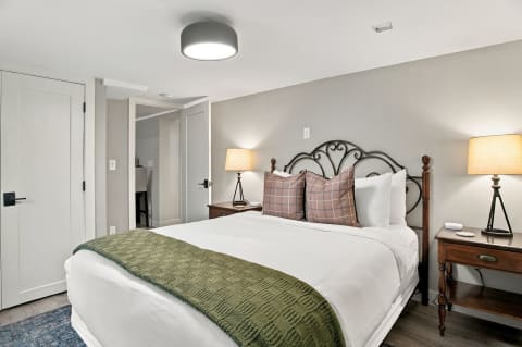 Cozy bedroom with a plush bed, white linens, plaid pillows, and warm bedside lighting.