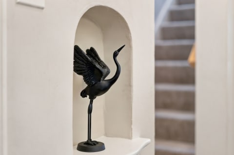 Black crane sculpture neatly placed in a white alcove beside a stairway.