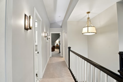 A well-lit hallway with gray walls, modern light fixtures, and plush carpet leading to a cozy area.