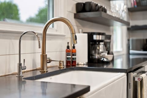 A modern kitchen showcasing a brass faucet, farmhouse sink, and sleek black granite countertops with open shelves.