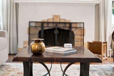 A beautifully designed coffee table with a brass vase and a coffee table book in front of a stone fireplace.