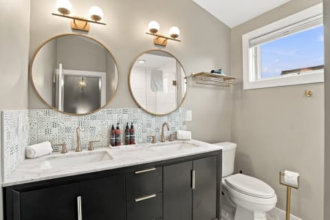 Modern bathroom with dual round mirrors, marble countertop, and stylish fixtures.