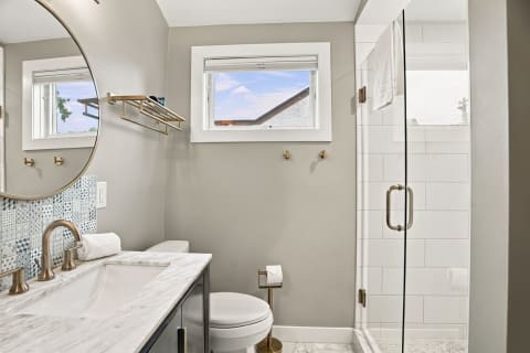 Modern bathroom featuring marble countertops, stylish brass fixtures, and a glass-enclosed shower.