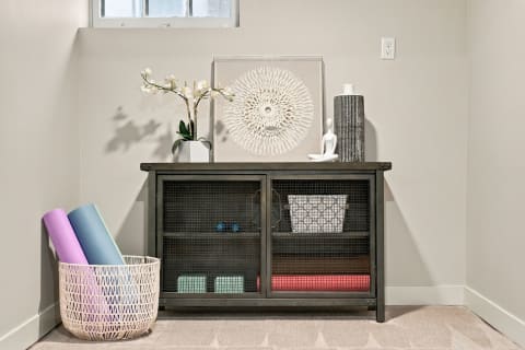 A wellness corner with a storage unit displaying yoga mats, an orchid, and a meditating figurine, creating a peaceful atmosphere.