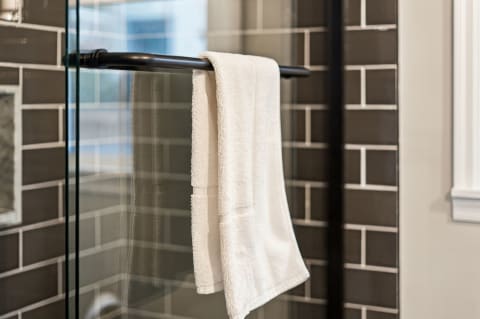 A white towel hanging on a black towel bar inside a glass shower with gray subway tiles in the background.