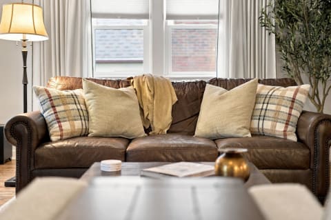 A cozy living room featuring a brown leather sofa with decorative pillows, a throw blanket, and a floor lamp.