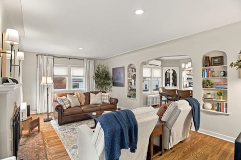 A stylish living room featuring a brown leather sofa, navy throw, and bright natural light from windows.