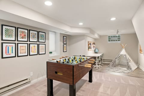 A game room with a foosball table, a play teepee, and a workspace featuring framed game art.