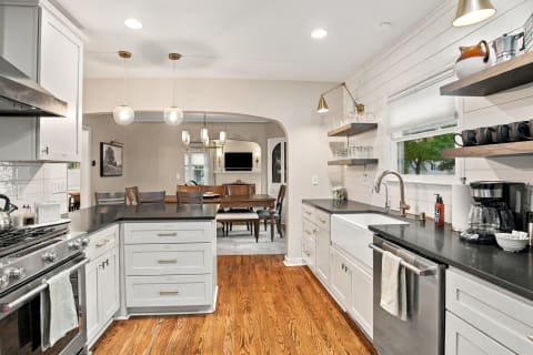Modern kitchen featuring white cabinets, dark countertops, and pendant lighting over a kitchen island, with a view of the dining area.