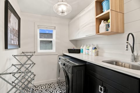 Bright laundry room with black washer, white countertops, and organized supplies.