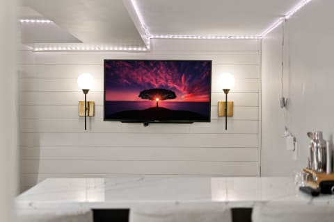 A cozy living room with a TV displaying a sunset, flanked by modern wall sconces and adorned with a marble table.