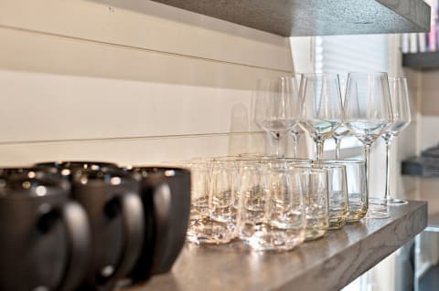 Neatly arranged drinkware including black mugs, tumblers, and wine glasses on a wooden shelf.