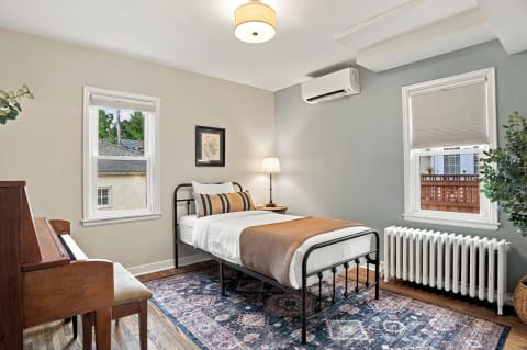 A cozy bedroom with a bed, piano, and windows that allow soft light in.