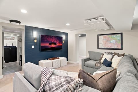 Cozy basement entertainment space featuring gray seating, a large TV, and a modern decor style.