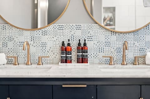 Stylish bathroom with dual vanities, gold faucets, patterned mosaic tiles, and decorative amber bottles.