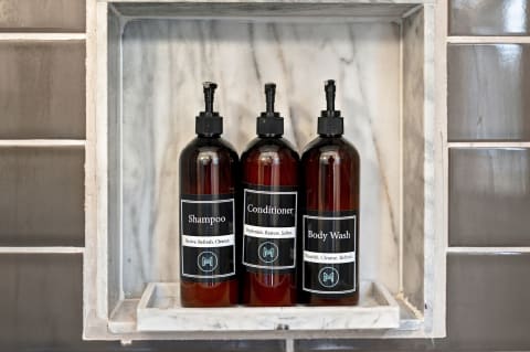 Three bottles of luxurious bath products labeled shampoo, conditioner, and body wash in a marble niche against stylish bathroom tiles.