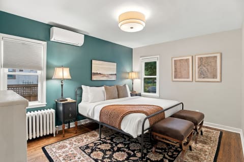 Inviting bedroom featuring a plush queen bed, teal wall, vintage radiator, and modern climate control unit.
