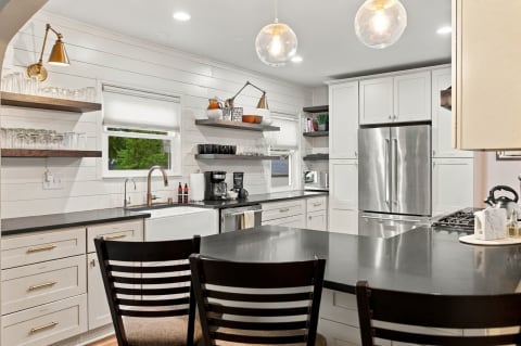 Kitchen featuring black granite countertops, white cabinets, stainless steel appliances, and open shelving with glassware.