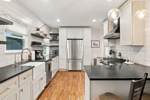 Modern gourmet kitchen with stainless steel appliances, black countertops, and open shelving.