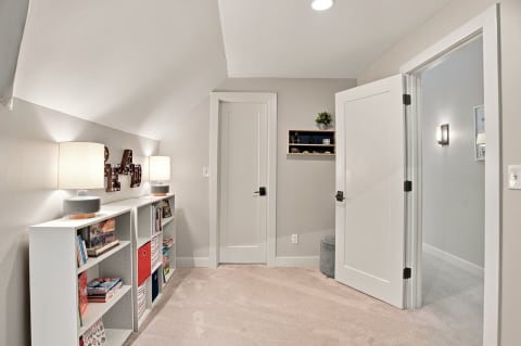 A well-decorated hallway with vaulted ceilings, shelf with books, and two doors.