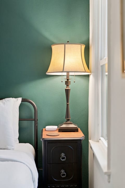 A cozy bedroom featuring a black metal bed, teal walls, and a vintage lamp on a wooden nightstand, creating a tranquil reading nook.